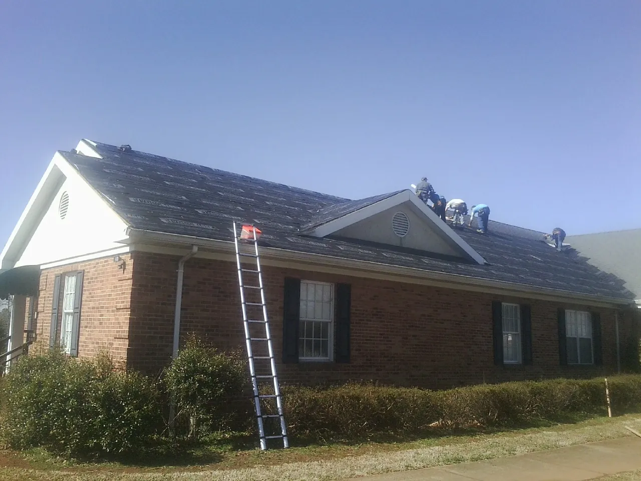 Crew tearing shingles off a brick ranch roof with a ladder set — Metal Roof Repair work by our crew in Stanardsville