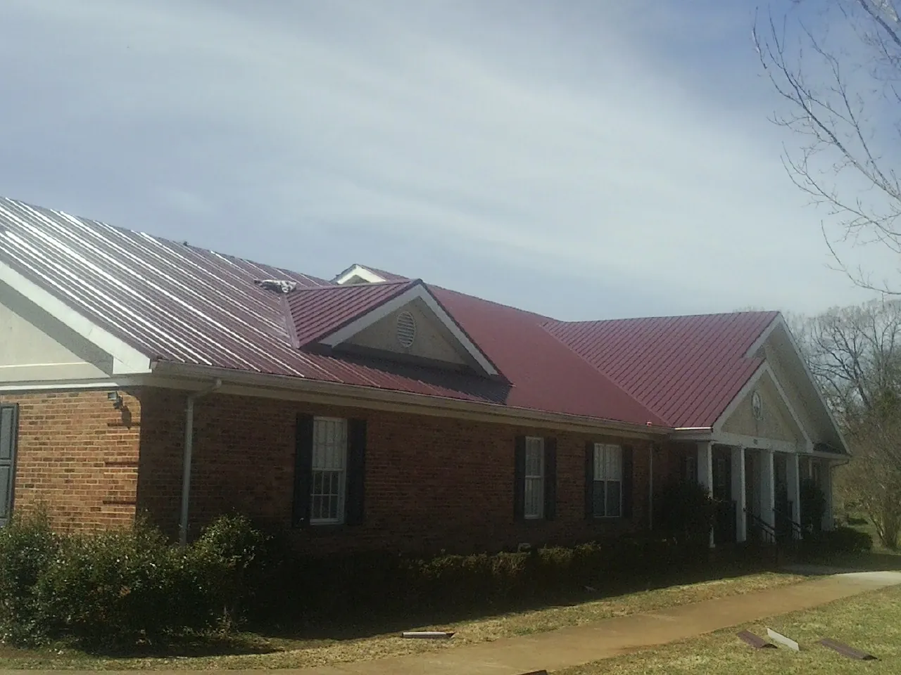 Red metal roof with gabled entries on a long brick building, from a Hail Damage Roof Repair job in Stanardsville