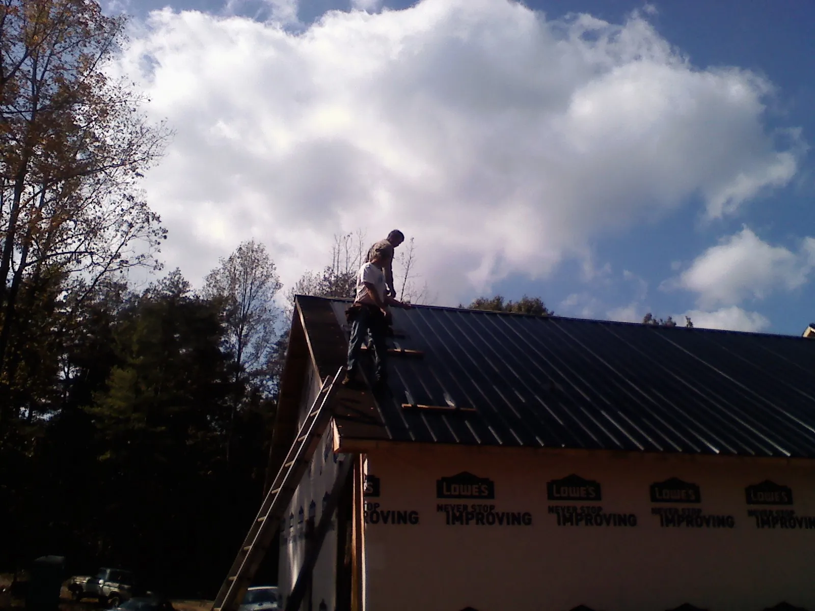 Roofer fastening dark metal panels high against a cloudy sky, from a Roof Inspection job in Stanardsville