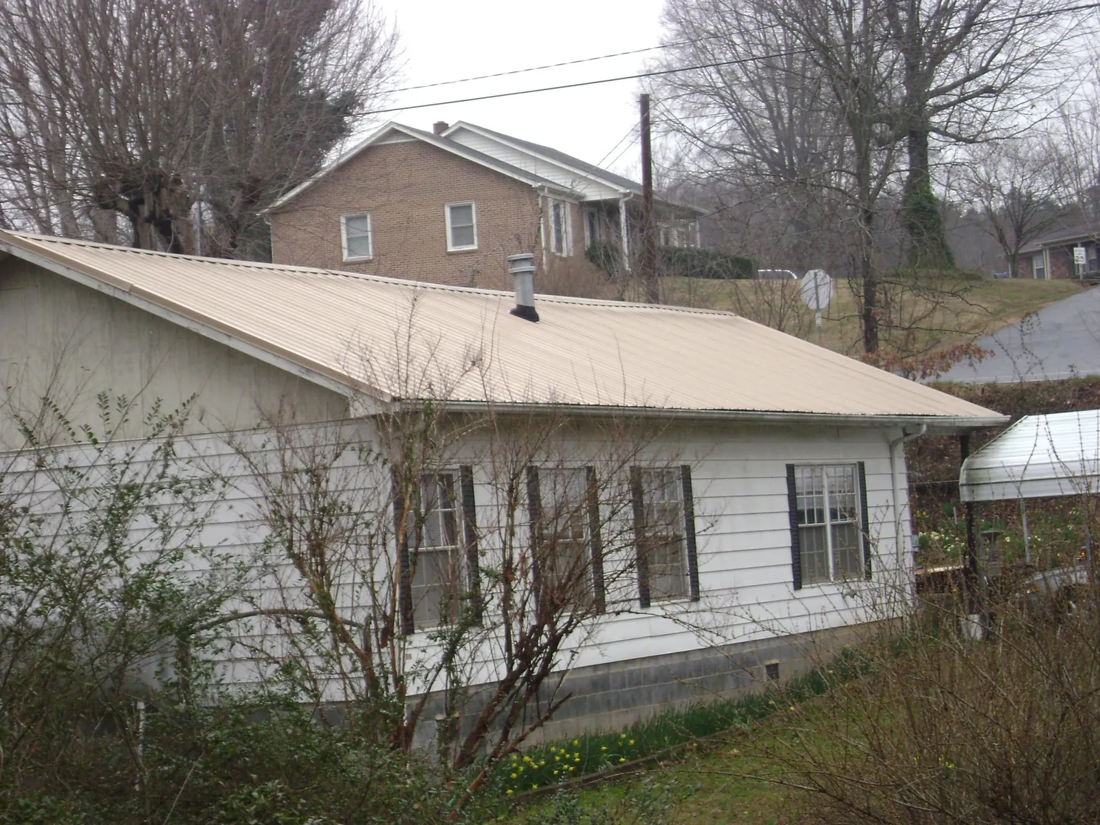 Tan metal roof on a white sided house set into a hillside — Commercial Roofing by Roofing Brothers in Stanardsville